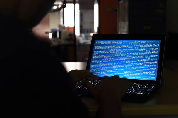 Computerhackersilhouette tippt am Computer in einem dunklen Raum. Arbeit an blauer Binärcodetechnologie. binäre Daten, Computerprogrammierung und Netzwerksicherheitskonzepte. - Foto, Bild