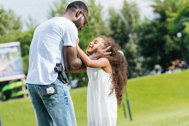 афро-американський поліцейський і дочка обіймається в парку розваг
 - Фото, зображення