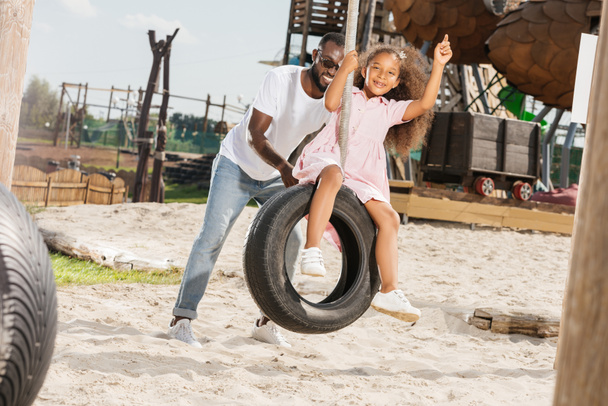 africano americano padre empujando hija en neumático swing en parque de atracciones
 - Foto, imagen