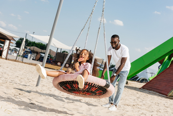 feliz afroamericana hija con piruleta en araña web nido swing en parque de atracciones
  - Foto, imagen