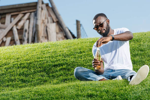 όμορφος αφρικανική αμερικανική άνθρωπος άνοιγμα μπουκάλι σόδα σε καταπράσινο λόφο - Φωτογραφία, εικόνα