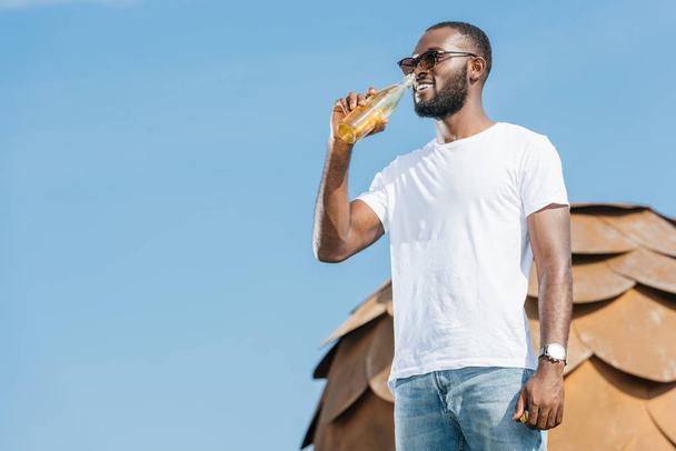 smiling handsome african american man drinking soda against blue sky - Zdjęcie, obraz