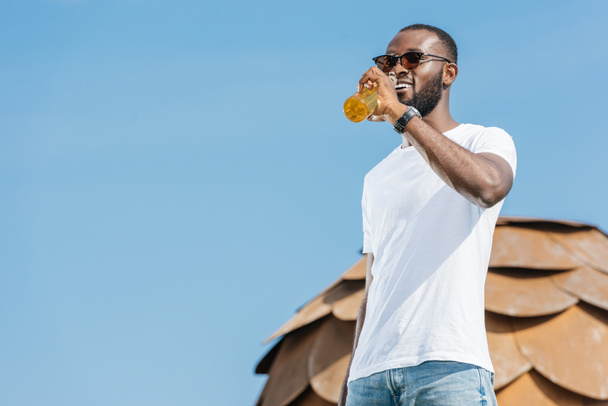 handsome african american man drinking beverage against blue sky - Photo, image