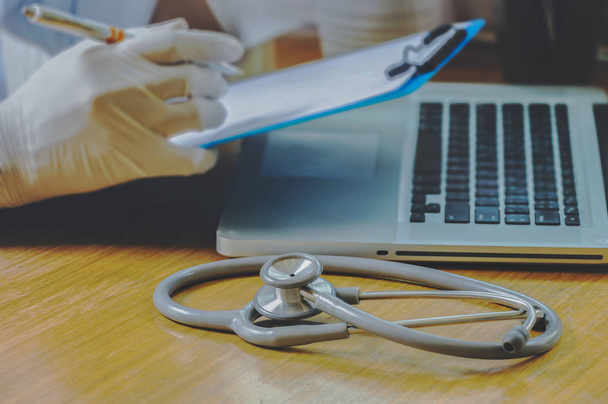 Stethoskop mit Klemmbrett und Laptop auf dem Schreibtisch, im Krankenhaus arbeitender Arzt schreibt ein Rezept, Gesundheits- und Medizinkonzept, Testergebnisse im Hintergrund, Vintage-Farbe, selektiver Fokus - Foto, Bild