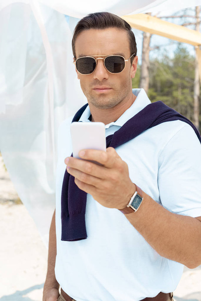 portrait of handsome man in sunglasses using smartphone - Fotoğraf, Görsel