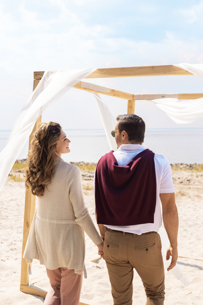 rear view of happy couple on sandy beach with white curtain lace decoration - Photo, Image