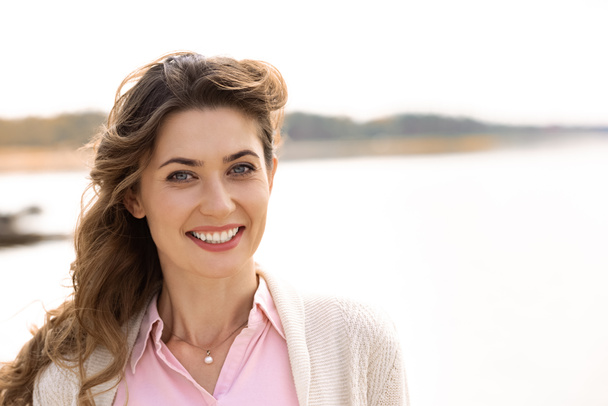 portrait of beautiful smiling woman with looking at camera river on background - Photo, Image