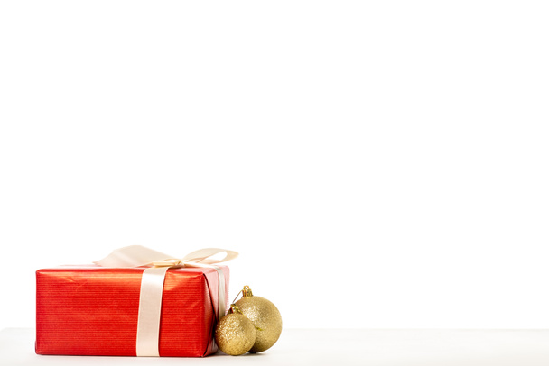 gift box wrapped by ribbon and golden christmas baubles on white background  - Foto, afbeelding