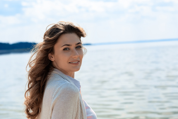 side view of beautiful woman looking at camera with river on background - Fotografie, Obrázek