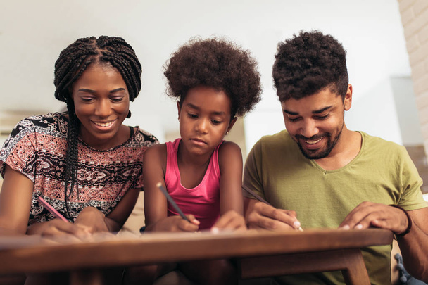 Mom and dad drawing with their daughter. African american family spending time together at home. - Фото, изображение