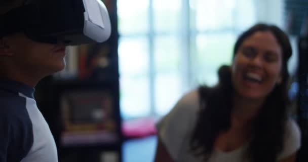 Captura de cerca de cámara lenta de una mujer sonriendo mientras ve a su hijo jugar con gafas de realidad virtual en casa. Al final del disparo el niño cae al suelo
. - Imágenes, Vídeo
