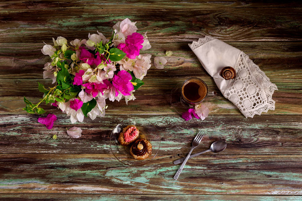Bodegón con dos pasteles pequeños "roxakia" con jarabe en un plato, un ramo de flores y una taza de café de cerca sobre un fondo de madera (cocina griega
) - Foto, Imagen