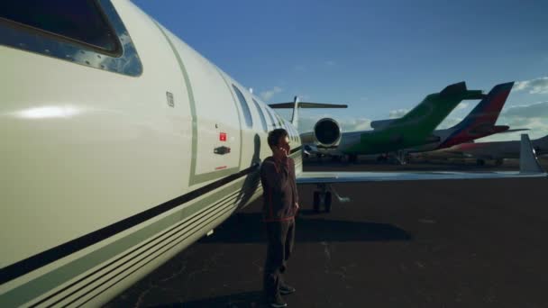Foto diurna de un hombre hablando en su teléfono móvil mientras está parado justo en frente de un avión privado
 - Imágenes, Vídeo