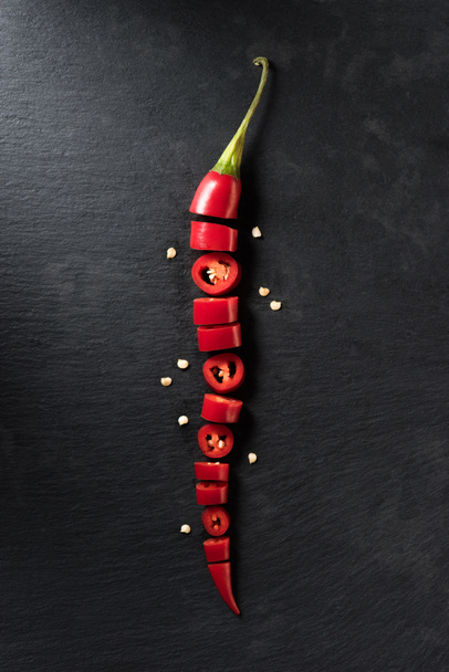 top view of cut red ripe chili pepper on black surface  - Foto, Imagem