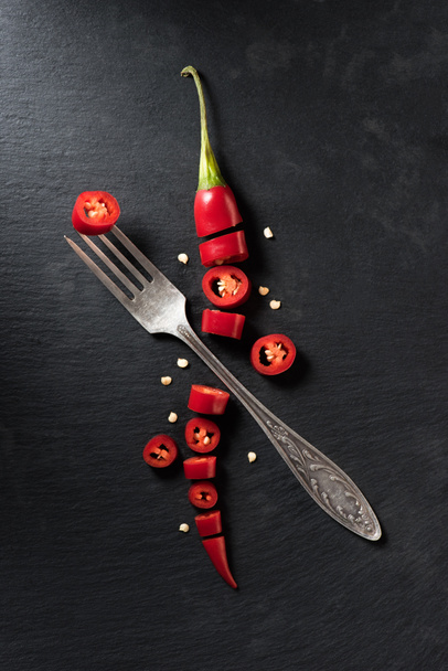 elevated view of cut red ripe chili pepper and fork on black surface - Photo, Image