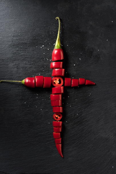 υπερυψωμένη θέαση των δύο κόκκινα ώριμα πιπέρια τσίλι κοπεί σε μαύρη επιφάνεια - Φωτογραφία, εικόνα