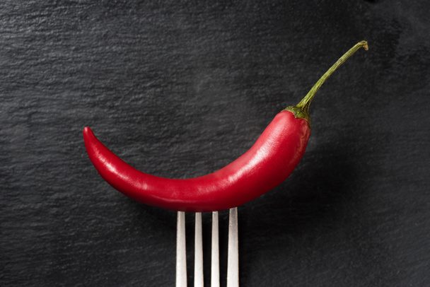 top view of red ripe chili pepper on fork on black surface - Foto, immagini