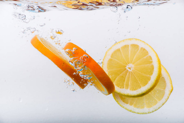 Slices of fresh orange and lemon in water with bubbles. Sparkling water. Freshness. Citrus fruits in water. - Photo, Image