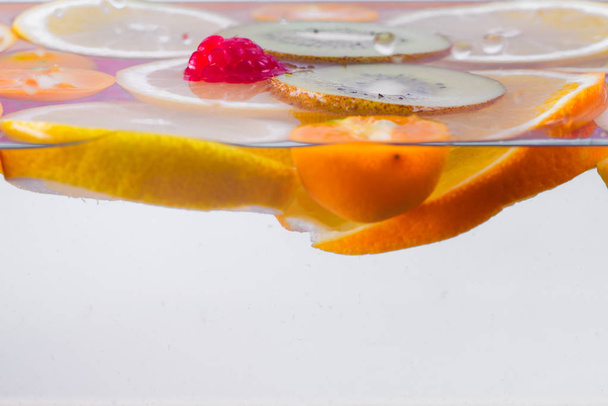 Fresh kiwi, tangerine, raspberry and orange and lemon slices floating on water surface. Freshness. Citrus fruits in water. - Foto, Bild