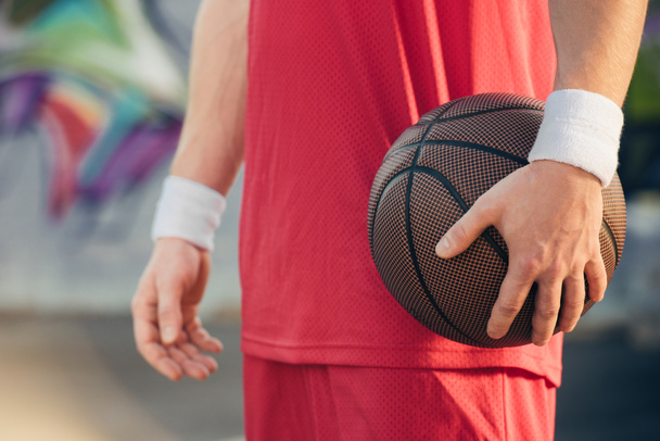 image recadrée d'un joueur de basket en tenue de sport rouge tenant un ballon de basket dans la rue
 - Photo, image