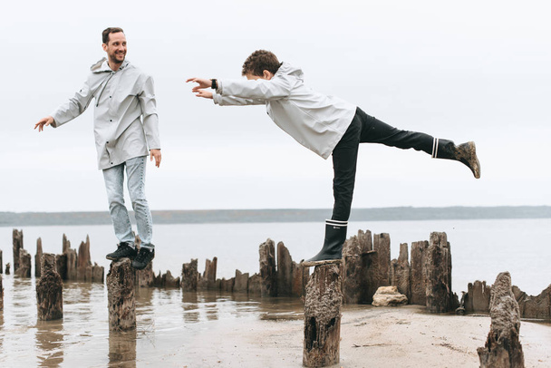 Father and son have a fun and doing joga exersises in raincoart near the sea - Fotoğraf, Görsel