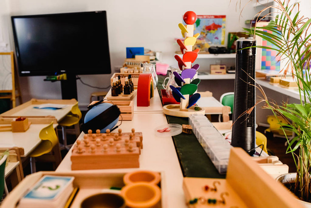 Стол и стеллажи с материалом Монтессори, цветными предметами и деревянными цилиндрами для изучения геометрии в классе
. - Фото, изображение