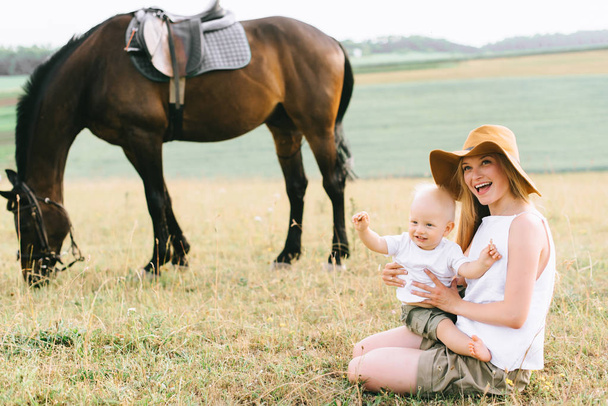 young woman and baby boy have a fun in the field. Parent and child with a horse in the field  - Photo, Image