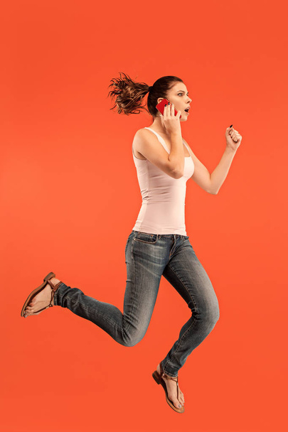 Full length of pretty young woman with mobile phone while jumping - Photo, Image