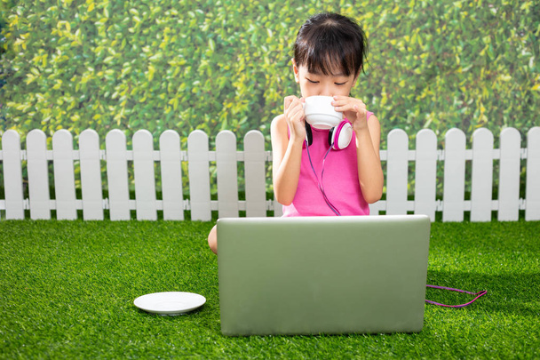 Asian Little Chinese girl sitting on the grass and playing with laptop at outdoor park - Photo, image