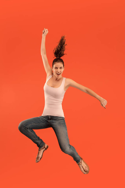 Libertad de movimiento. Mujer bastante joven saltando sobre fondo naranja
 - Foto, Imagen