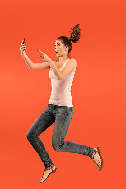 Image of young woman over blue background using laptop computer or tablet gadget while jumping. - Fotoğraf, Görsel