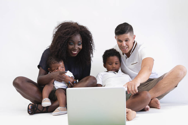 Mixer race family sitting on floor with 2 children. Couple sitting on floor with two sons and watching laptop. Isolated. Multi ethnic family concept. - Photo, image
