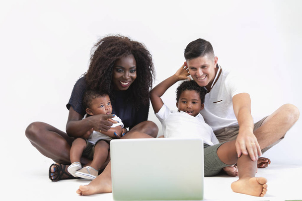 Mixer race family sitting on floor with 2 children. Couple sitting on floor with two sons and watching laptop isolated. - Φωτογραφία, εικόνα
