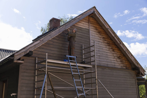 Senior baut Haus, indem er auf Baugerüst steht - Foto, Bild