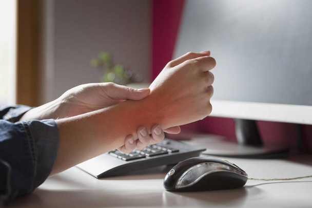 Toimisto-oireyhtymä - Nuori nainen kärsii käsi kipua käyttäessään tietokonetta työpaikalla. Ammatillinen riskitekijä. Terveydenhuolto ja lääketieteellinen käsite. - Valokuva, kuva
