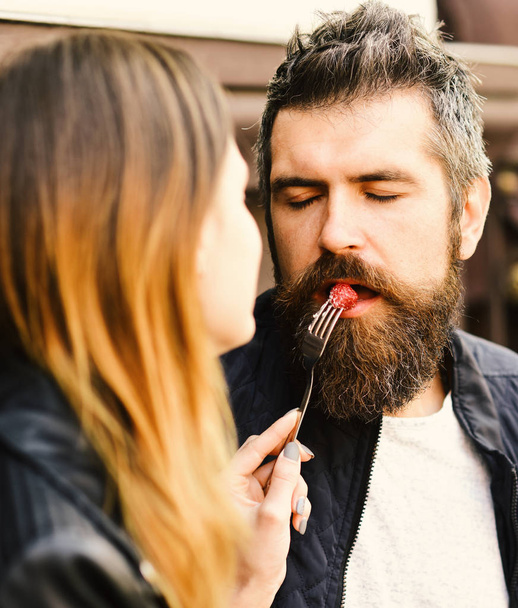 Girl feeds bearded guy with raspberry on fork - Φωτογραφία, εικόνα