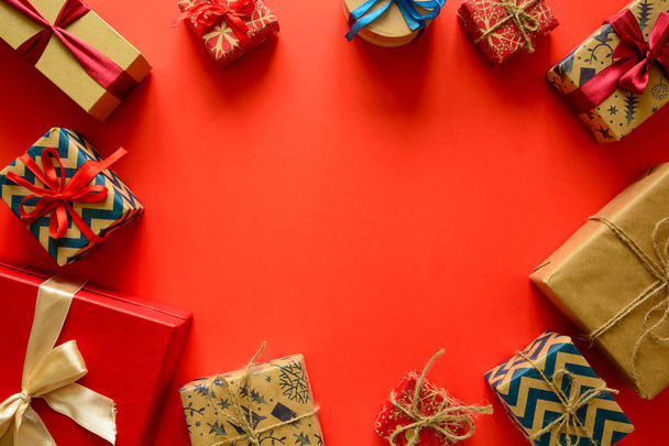 Pohled shora na vánoční dárky zabalený do dárkového papíru zdobené stužkou na červené papírové pozadí. Nový rok, svátky a oslavy dekorace koncept. Kopírovat prostoru. Rozložení bytu - Fotografie, Obrázek
