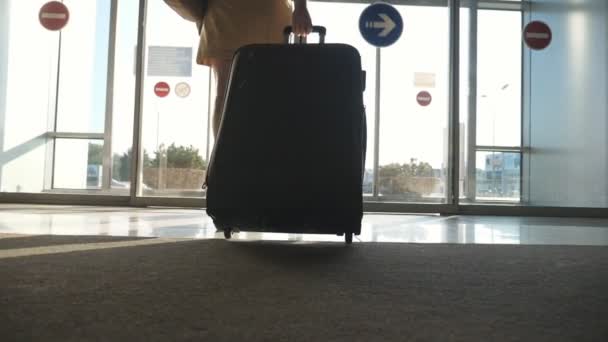 Vrouw in hakken gaat naar de uitgang van de luchthaven en roll koffer op wielen. Meisje lopen met haar koffer langs luchthaven hall of wachtkamer. Zakelijke dame gaat met haar bagage. Travel concept Slowmotion - Video