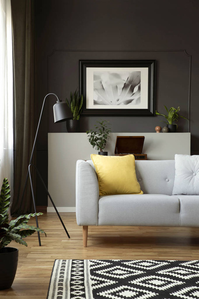Yellow cushion on grey sofa next to lamp in scandi living room interior with poster. Real photo - Photo, Image