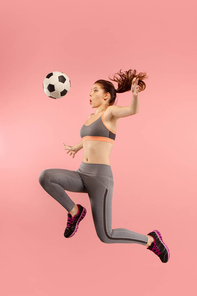 Forward to the victory.The young woman as soccer football player jumping and kicking the ball at studio on a red - Photo, image