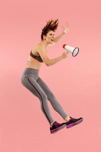 Mooie jonge vrouw springen met megafoon geïsoleerd op rode achtergrond - Foto, afbeelding