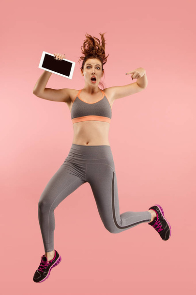 Image of young woman over blue background using laptop computer or tablet gadget while jumping. - Photo, Image