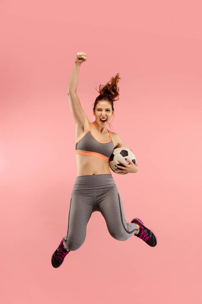 Forward to the victory.The young woman as soccer football player jumping and kicking the ball at studio on a red - Foto, Imagen