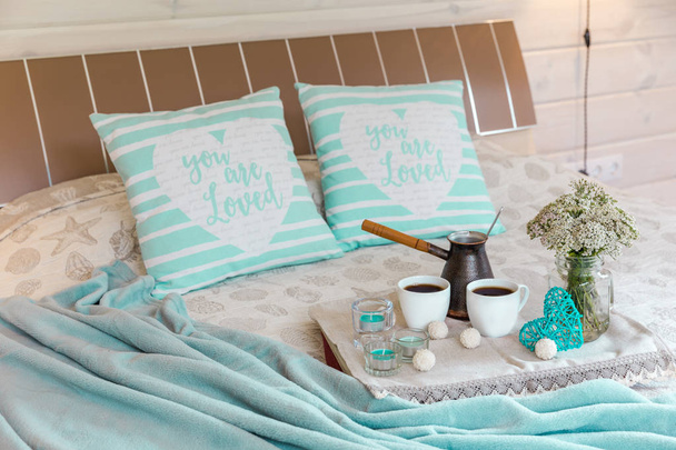 Un acogedor dormitorio con tazas de café, flores silvestres en una tabla de madera en la cama en casa. Desayuno romántico, descanso, relajación, amor. Casa de madera
 - Foto, Imagen