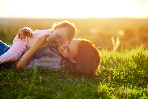 Matka a dcera ležela na trávě v poli při západu slunce. - Fotografie, Obrázek