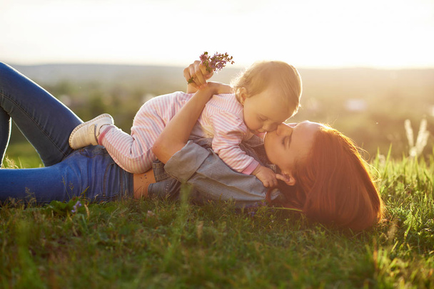 Young mother kissing little daughter lying on grass. - Fotoğraf, Görsel