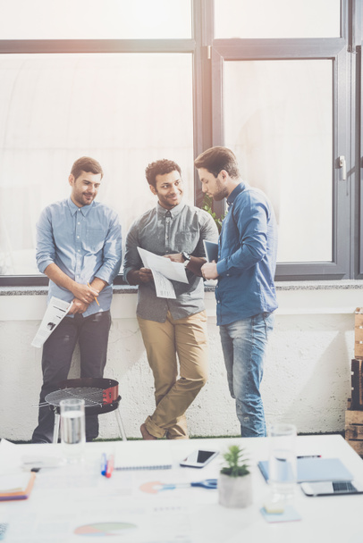 drei junge Geschäftsleute stehen zusammen und diskutieren Papiere, Teamwork-Konzept für Unternehmen - Foto, Bild