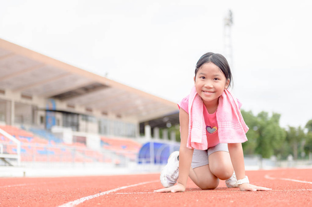 Мила дівчина на початковій позиції готова до бігу. дитячий спортсмен збирається почати спринт, дивлячись на камеру з яскравим сонячним світлом. концепція дієти та фізичних вправ
 - Фото, зображення
