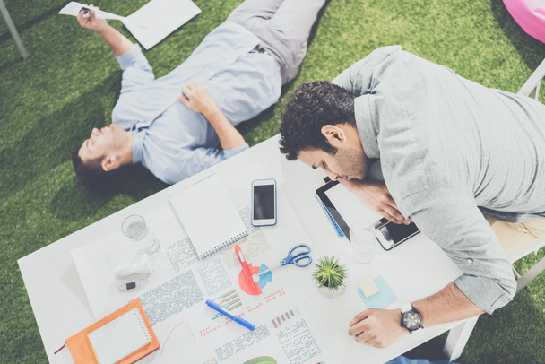 Jóvenes hombres de negocios durmiendo en la mesa y alfombra de hierba verde en la oficina moderna, trabajo en equipo de negocios
 - Foto, Imagen
