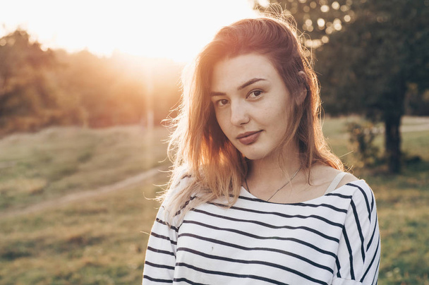 Young woman relaxing in summer sunset sky. Portrait of Beautiful Young Woman Backlit at Sunset Outdoors. Soft warm sunny colors. - Photo, Image